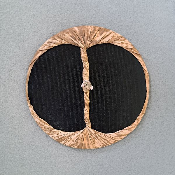 A baren: a disc of layered paper wrapped in bamboo sheath, with the twisted sheath forming a cord handle across the centre.