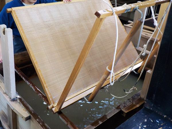 Paper-making: a craftsman lifting a screen of wet kozo fibre from a vat of water.